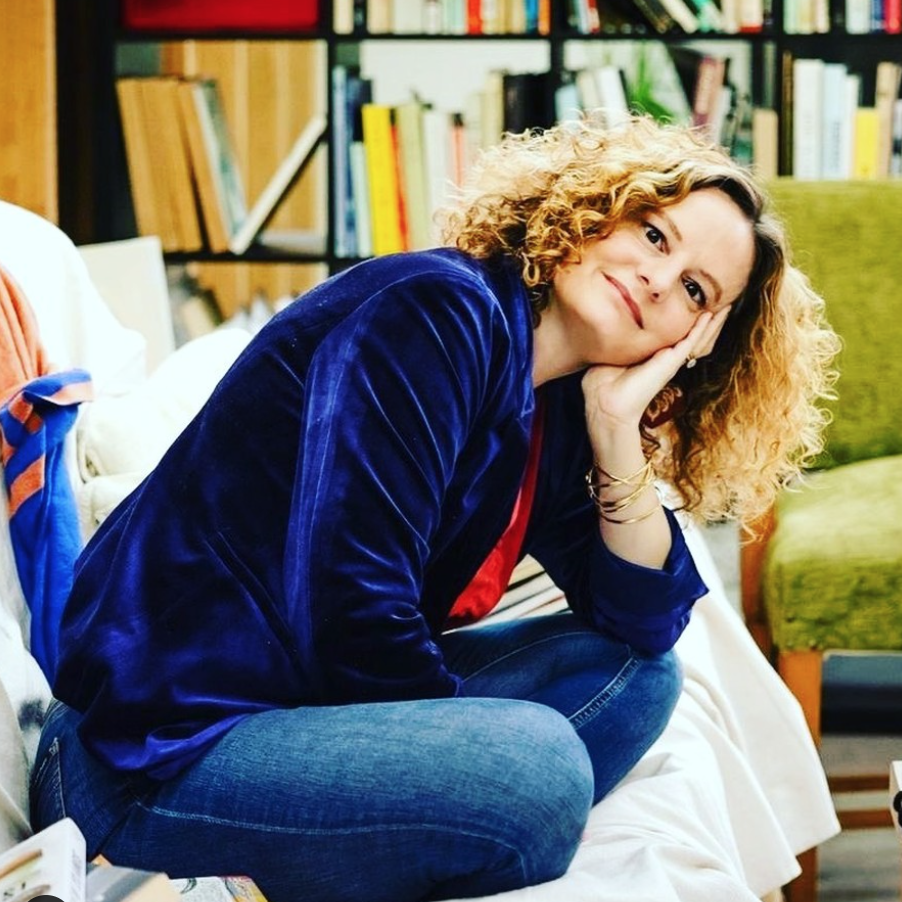 A photo of author Felicity Castagna sitting cross legged on a couch.